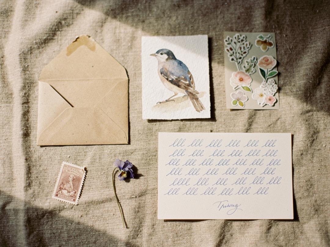 Flat lay: envelope, bird watercolor print, sticker sheet, handwritten practice card, violet, stamp